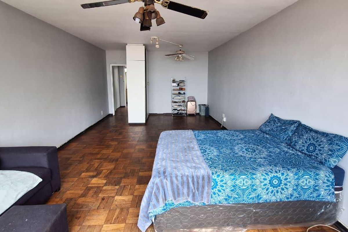 Spacious bedroom featuring classic parquet flooring, dual ceiling fans, and a built-in cupboard, offering a versatile layout for comfortable living.
