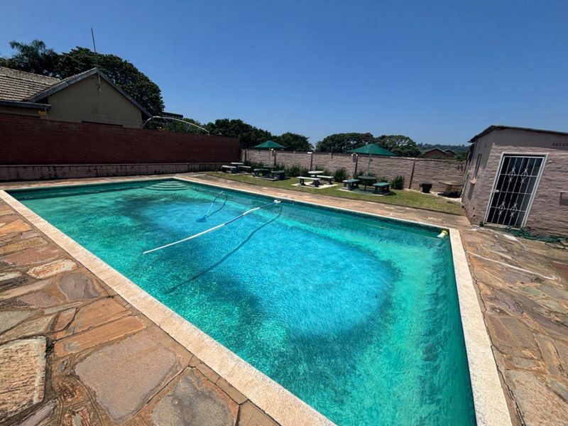 Outdoor pool area featuring stone paving, perimeter walling, and an adjacent outbuilding, requiring maintenance to the pool surface and surrounding finishes.