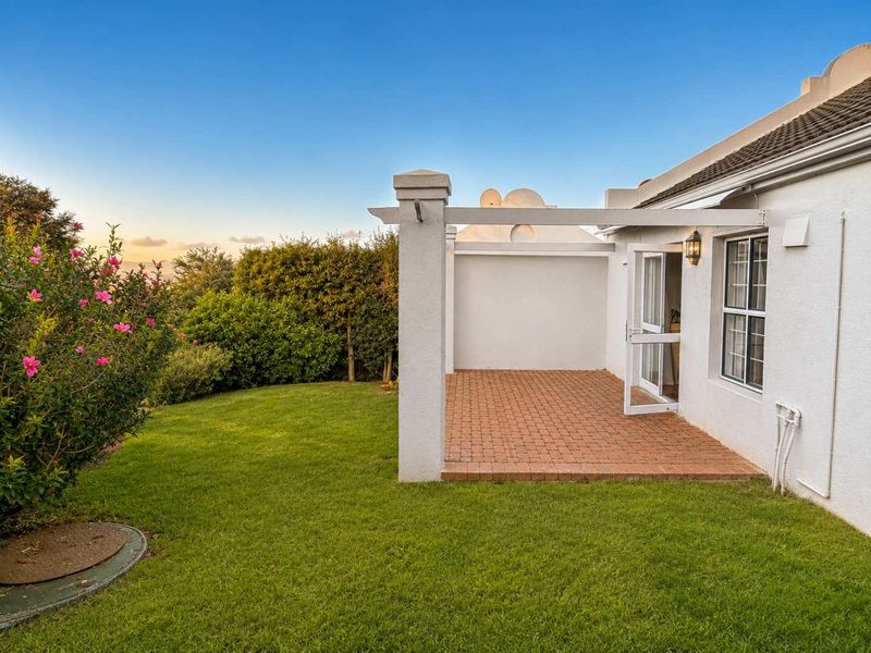 A well-maintained brick paved patio area featuring a pergola, accessible via a sliding glass door, overlooking a landscaped garden.