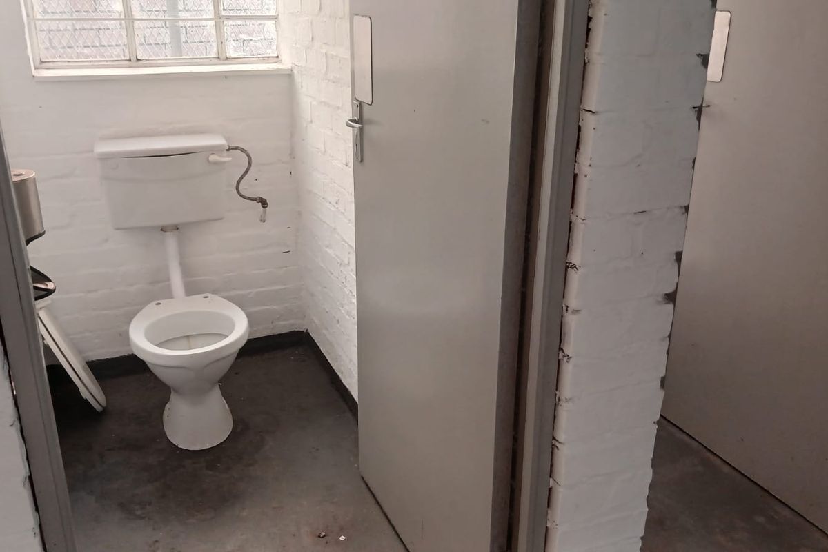 A basic industrial-style bathroom featuring a standard toilet, exposed brick walls, and a concrete floor, requiring cosmetic updates and maintenance.