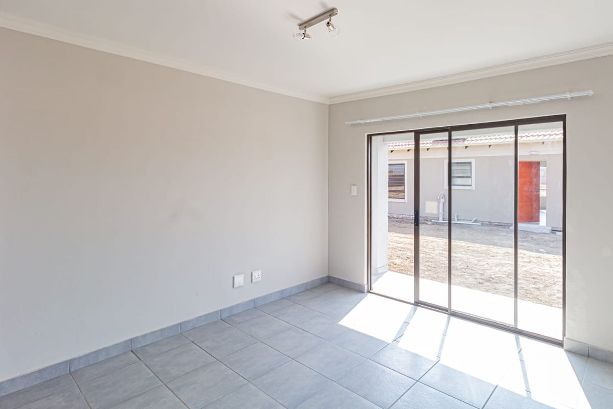 A bright, empty living room featuring neutral walls, tiled flooring, and large sliding glass doors that provide direct access to the rear exterior.