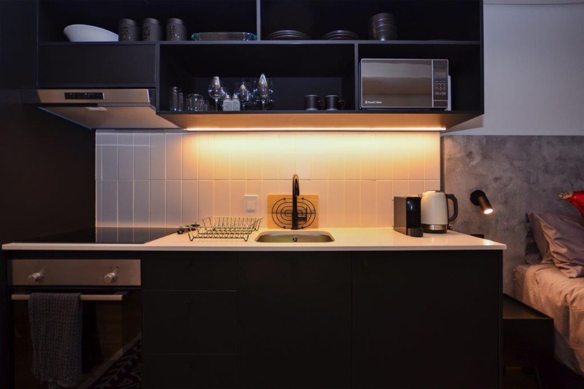 Modern compact kitchen featuring sleek black cabinetry, integrated appliances, tiled backsplash, and warm under-cabinet lighting, seamlessly integrated into the living space.