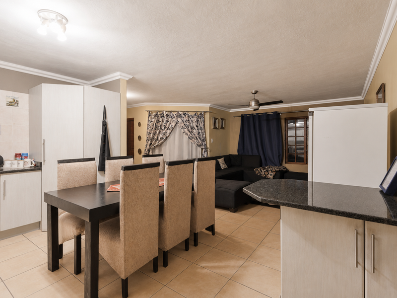 Open-plan living and dining area featuring tiled flooring, granite kitchen countertops, built-in cabinetry, and a ceiling fan.