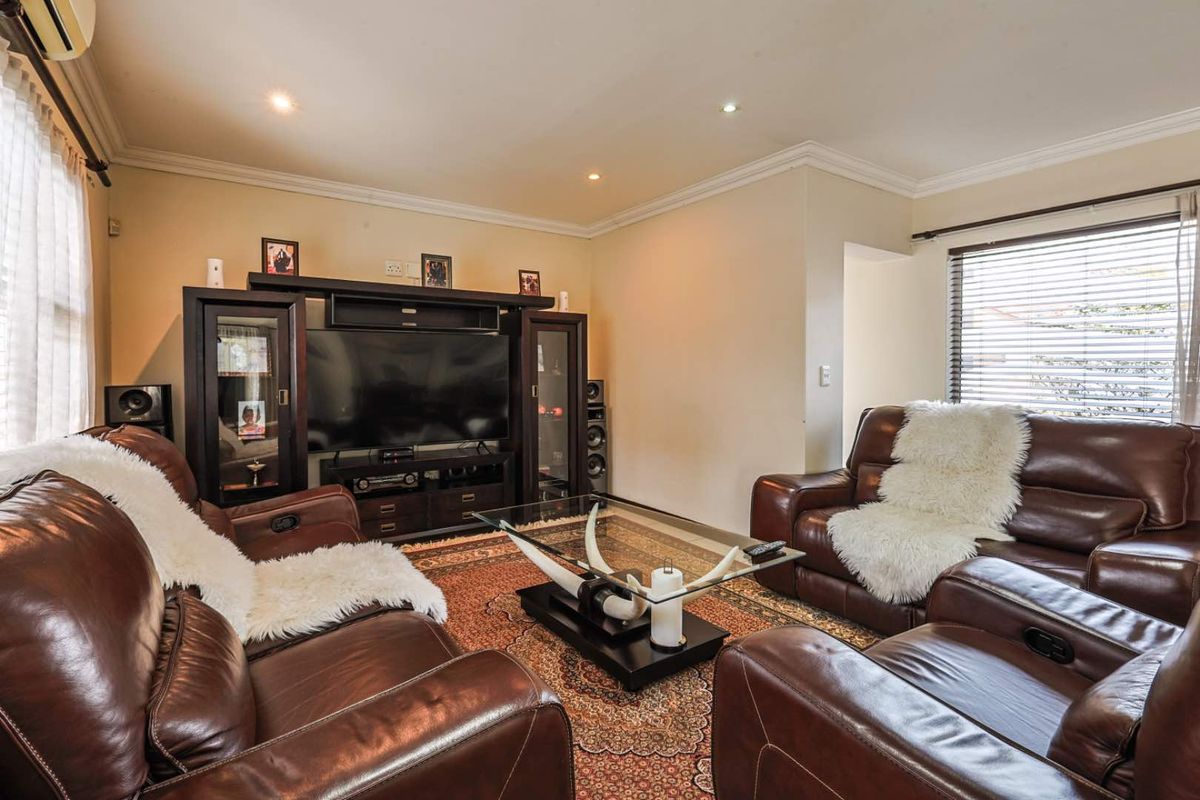 A comfortable living room featuring recessed downlighting, crown molding, and air conditioning, with large windows fitted with venetian blinds.