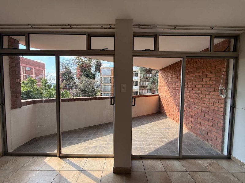 A spacious, empty balcony featuring exposed brick walls, tiled flooring, and large sliding glass doors providing access from the interior.