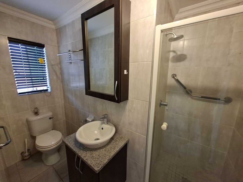A functional bathroom featuring a shower enclosure, vanity with granite countertop, vessel sink, and wall-mounted medicine cabinet with neutral wall and floor tiling.