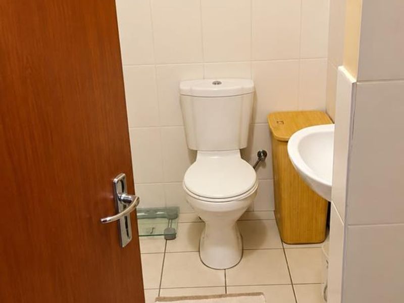 A functional bathroom featuring a standard toilet, wall-mounted washbasin, and neutral tiled finishes with a window providing natural light.