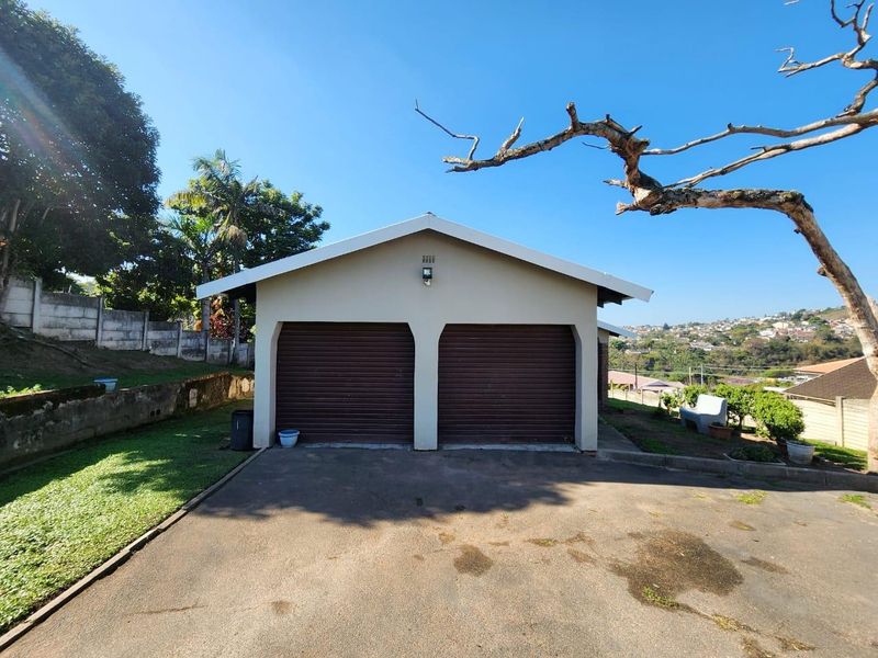 A detached double garage with roller doors, situated on a paved driveway with surrounding garden and retaining wall features.