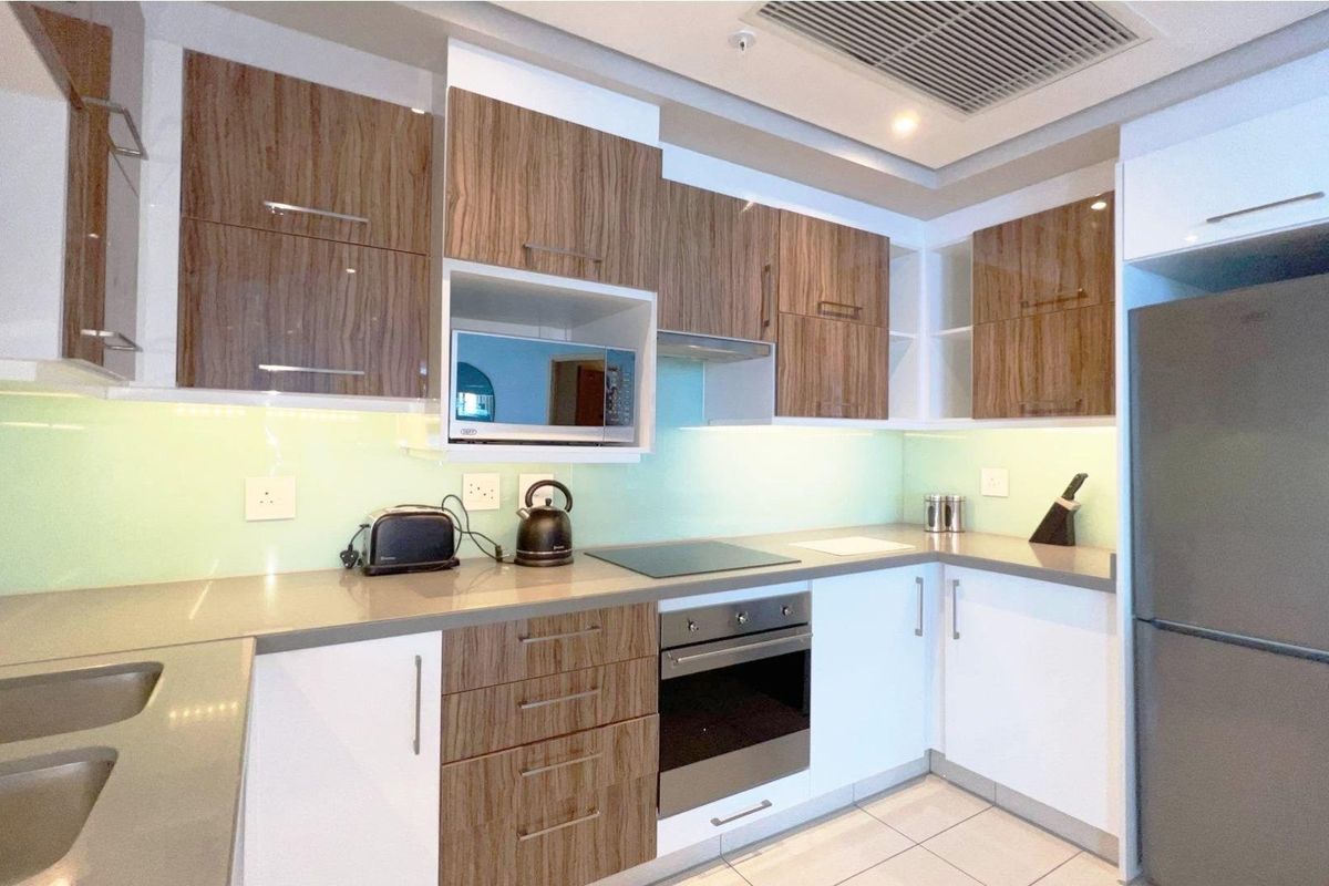 Modern kitchen featuring wood-grain and white cabinetry, stone countertops, integrated oven, electric cooktop, and a glass splashback.