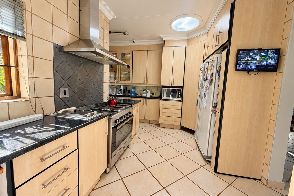 A functional kitchen featuring light wood cabinetry, granite countertops, a stainless steel gas stove with extractor, and tiled flooring with a skylight.