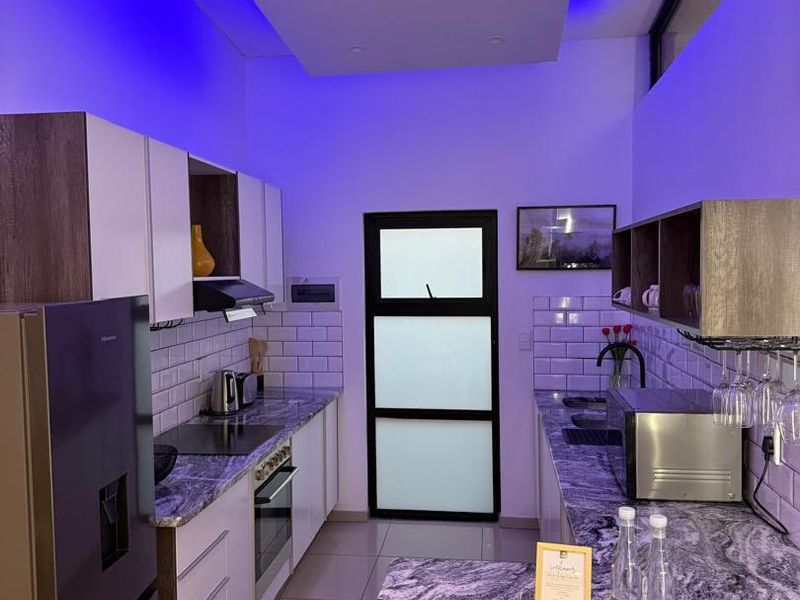 Modern kitchen featuring stone countertops, subway tile backsplash, built-in oven, hob, and integrated lighting with a contemporary glass panel door.
