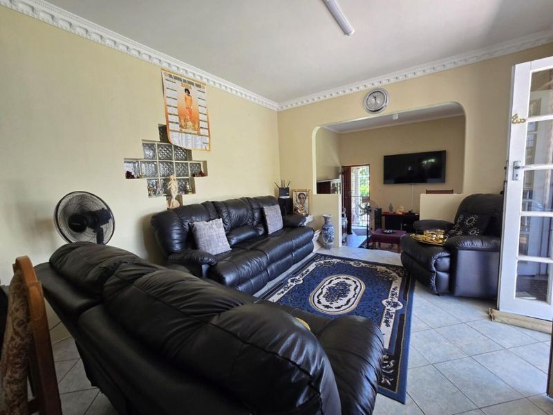 A living room featuring tiled flooring, decorative ceiling cornices, and a unique glass block feature wall, leading into an adjacent living space.