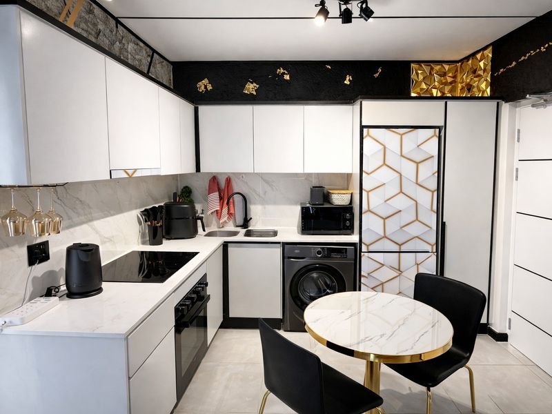 Modern kitchen featuring white cabinetry, marble-effect countertops, integrated appliances, and stylish black accents with contemporary track lighting.