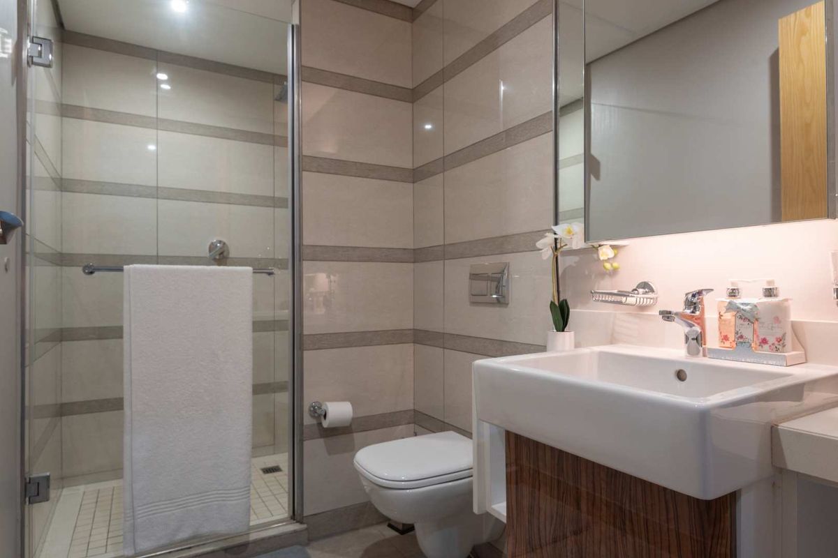 Modern bathroom featuring a glass-enclosed shower, wall-mounted toilet, and a sleek vanity with integrated basin and mirror.