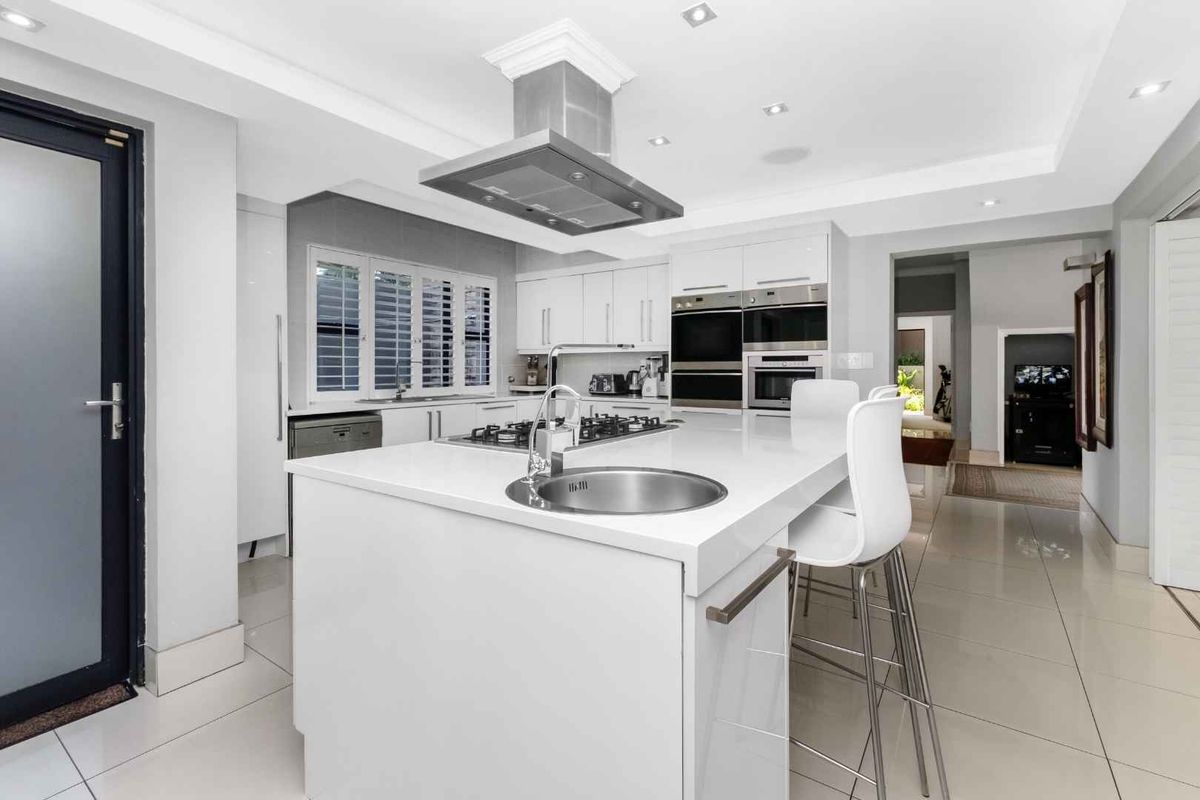 Modern kitchen featuring a central island with a prep sink, built-in double ovens, gas hob, stainless steel extractor fan, and sleek cabinetry.