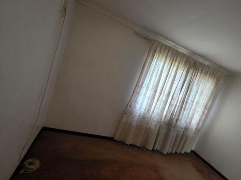 An empty bedroom featuring worn carpeting and existing curtain tracks, offering a blank canvas for renovation and interior design updates.