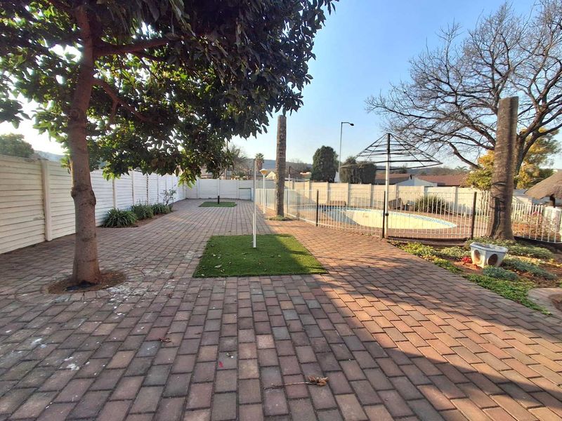 Spacious outdoor pool area featuring paved patio, perimeter walling, and a swimming pool with safety fencing, offering potential for an enhanced entertainment space.