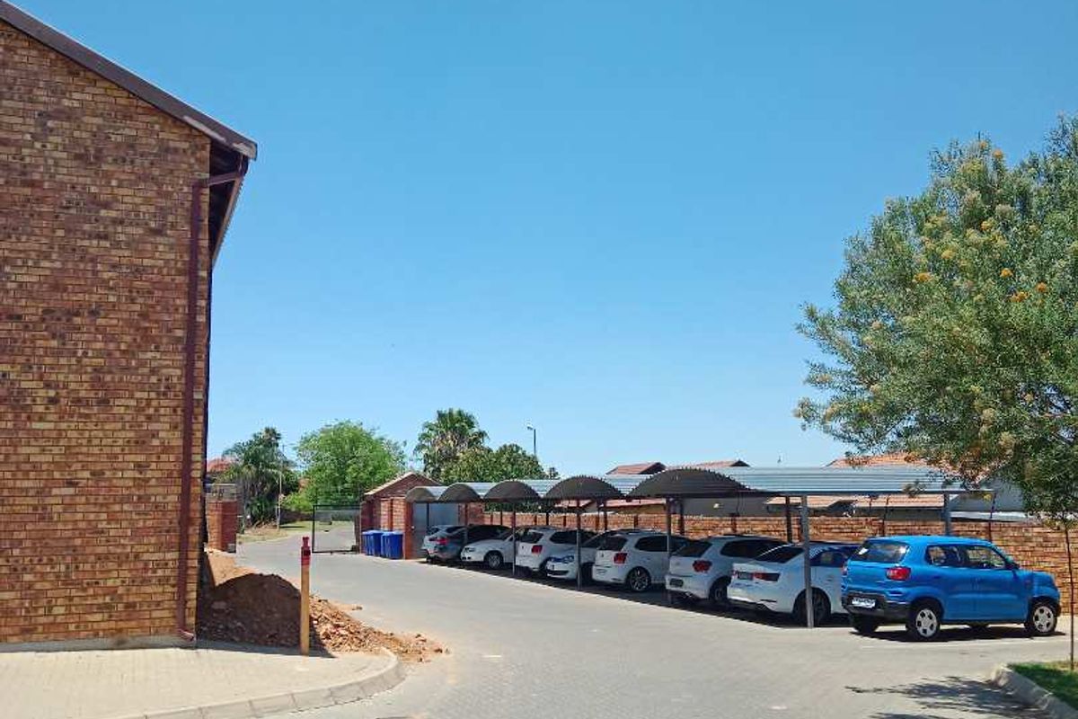 Exterior view of the apartment complex showing a brick building facade, paved driveway, and covered parking bays.