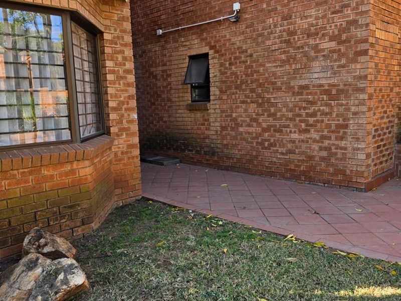 A view of the rear exterior featuring face brick walls, a tiled patio area, and security-fitted windows.