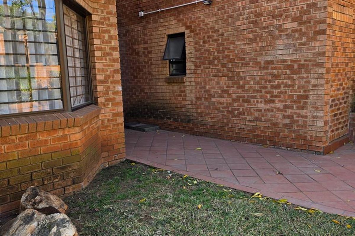 A view of the rear exterior featuring face brick walls, a tiled patio area, and security-fitted windows.