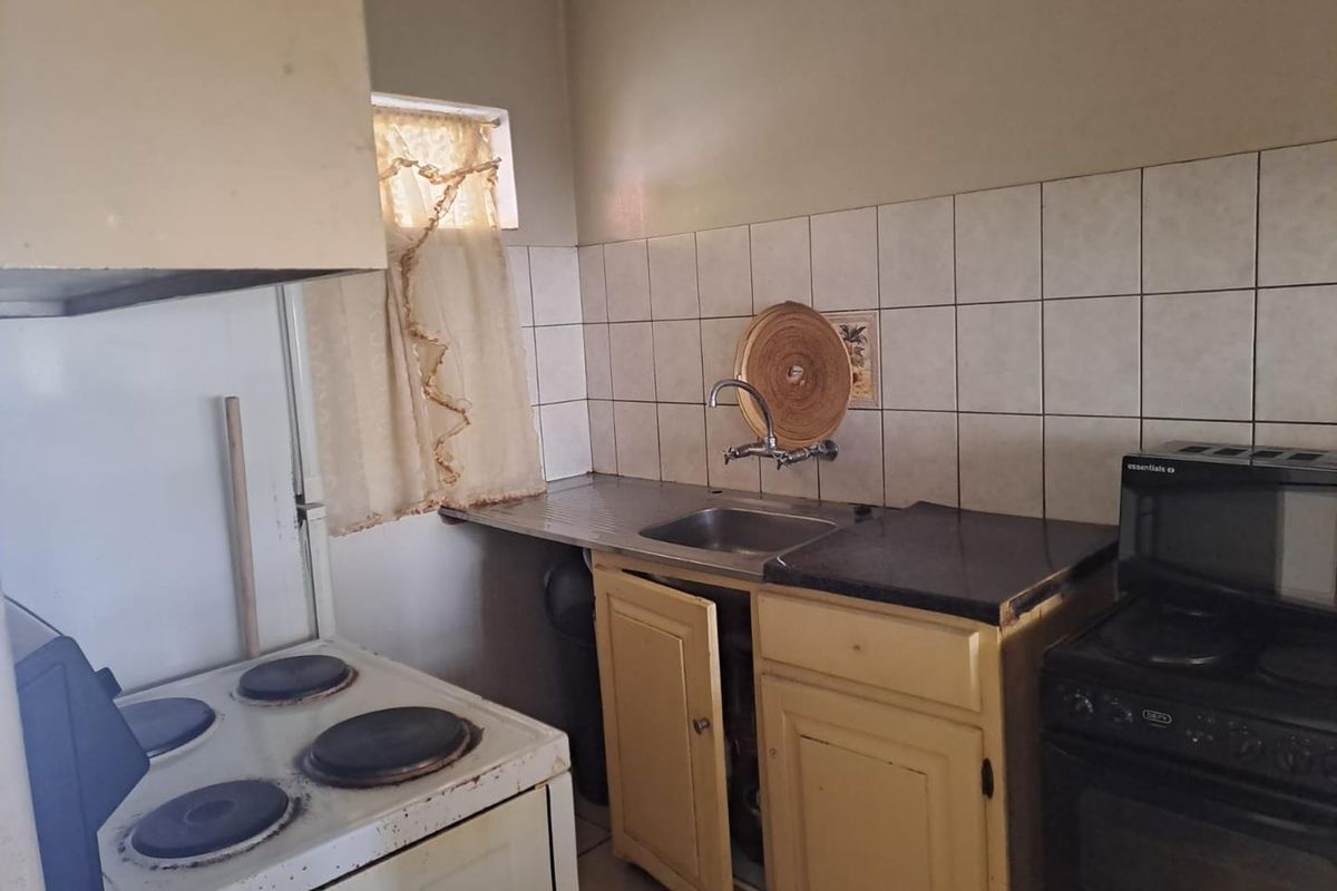 A compact kitchen featuring a stainless steel sink, tiled backsplash, and dated cabinetry, offering potential for a modern renovation.