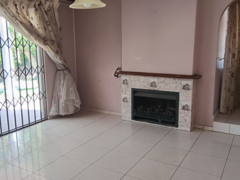 An empty living room featuring tiled flooring, a built-in fireplace with decorative tiling, and a security gate leading to the outdoor area.