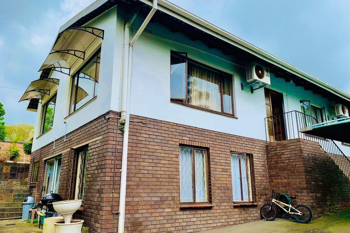 Two-story residential exterior featuring a combination of brick and painted plaster finishes, metal window awnings, and an external staircase.