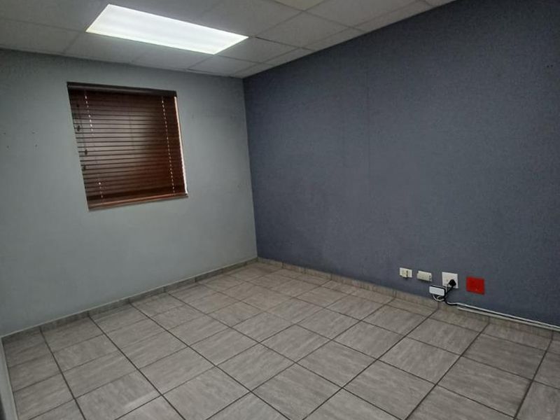 A vacant office space featuring tiled flooring, a drop ceiling with recessed lighting, and a window with fitted venetian blinds.