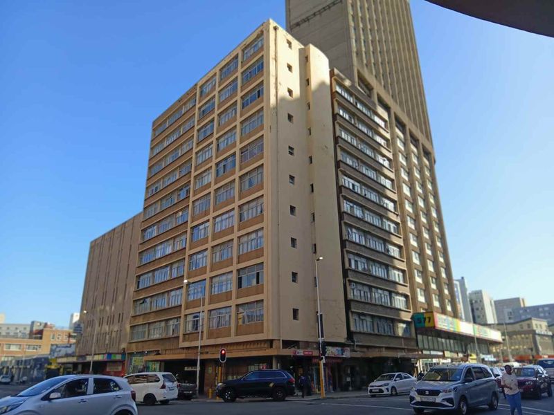 A multi-story apartment building featuring a grid window design and ground-level commercial space, situated on a busy urban street corner.