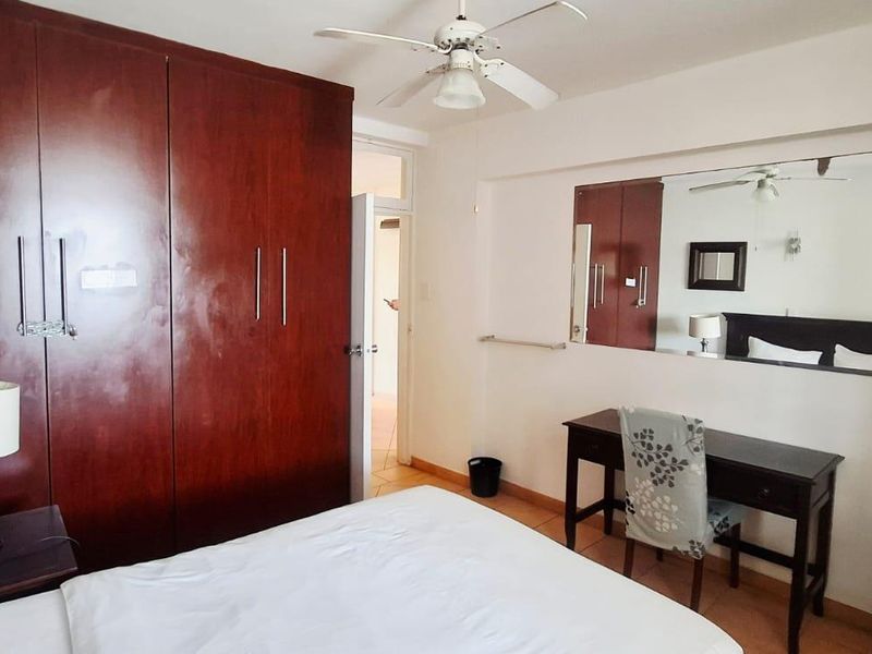 A bedroom featuring built-in wooden cupboards, a ceiling fan, and a large wall-mounted mirror, providing functional storage and classic finishes.