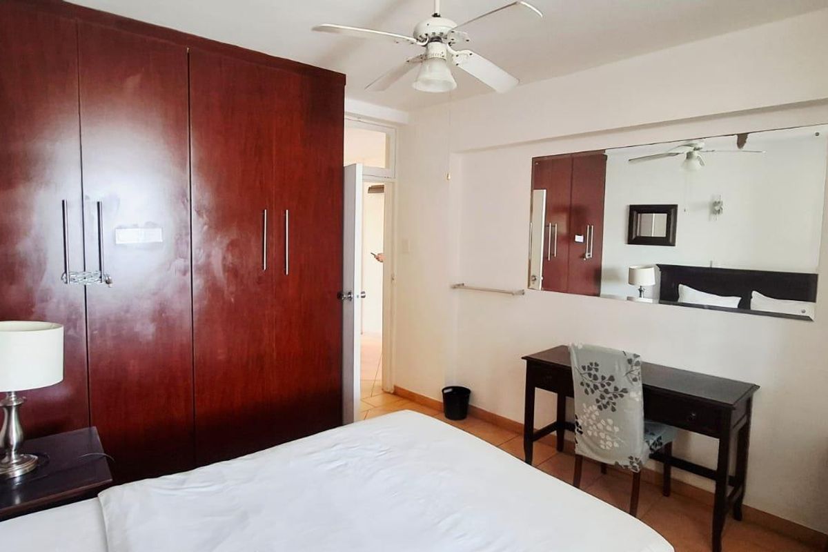 A bedroom featuring built-in wooden cupboards, a ceiling fan, and a large wall-mounted mirror, providing functional storage and classic finishes.