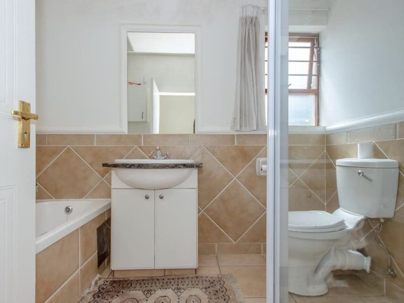 A functional bathroom featuring a vanity basin, bathtub, and toilet with neutral wall tiling and natural light from a side window.