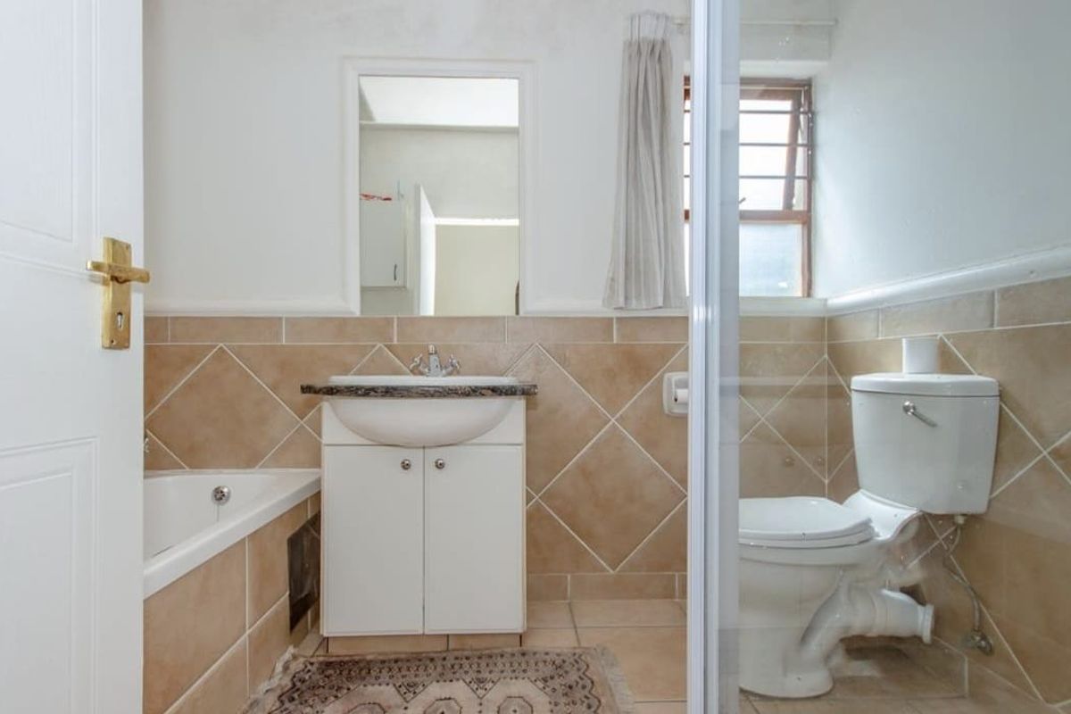 A functional bathroom featuring a vanity basin, bathtub, and toilet with neutral wall tiling and natural light from a side window.