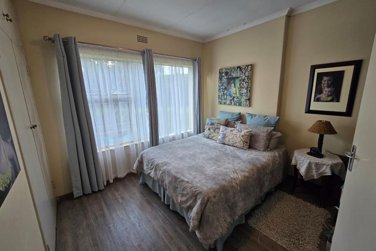 A functional bedroom featuring laminate flooring, a built-in wardrobe, and large windows that provide natural light.