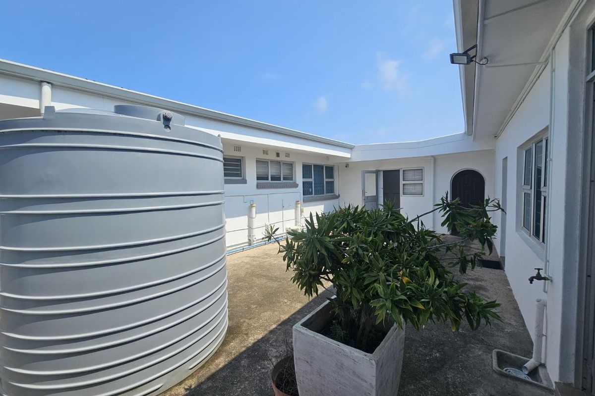 Rear courtyard area featuring a large water storage tank, concrete paving, and access to the main dwelling via security doors.