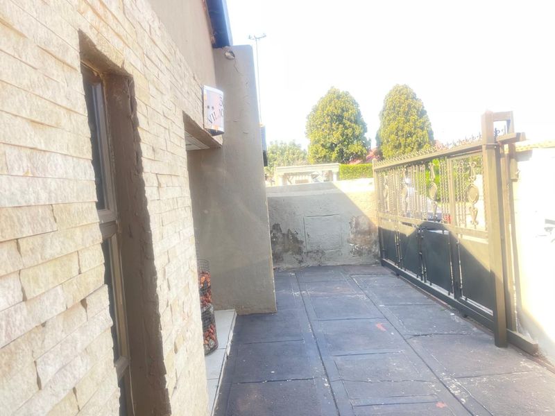 Front entrance area featuring stone cladding, a metal sliding gate, and a paved driveway with visible signs of wear and plaster damage.