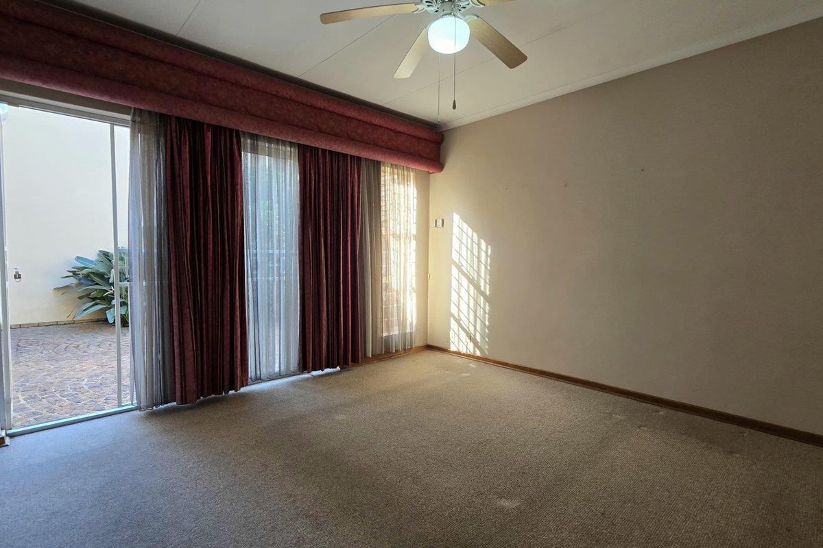 A spacious, empty bedroom featuring neutral walls, a ceiling fan, and large sliding glass doors providing direct access to an outdoor patio area.
