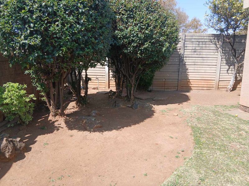 A private rear garden area featuring established shrubs, timber boundary fencing, and an outdoor water tap, requiring landscaping maintenance.