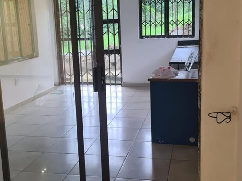 An empty living area featuring tiled floors, recessed lighting, and a sliding glass door with security bars, showing signs of unfinished maintenance.