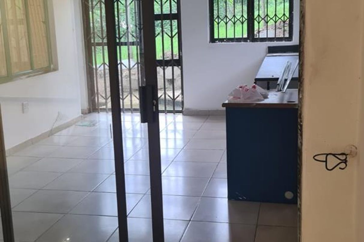 An empty living area featuring tiled floors, recessed lighting, and a sliding glass door with security bars, showing signs of unfinished maintenance.