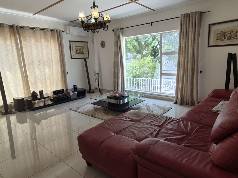 Spacious living room featuring polished tiled flooring, a split-system air conditioner, and large windows providing natural light and garden views.