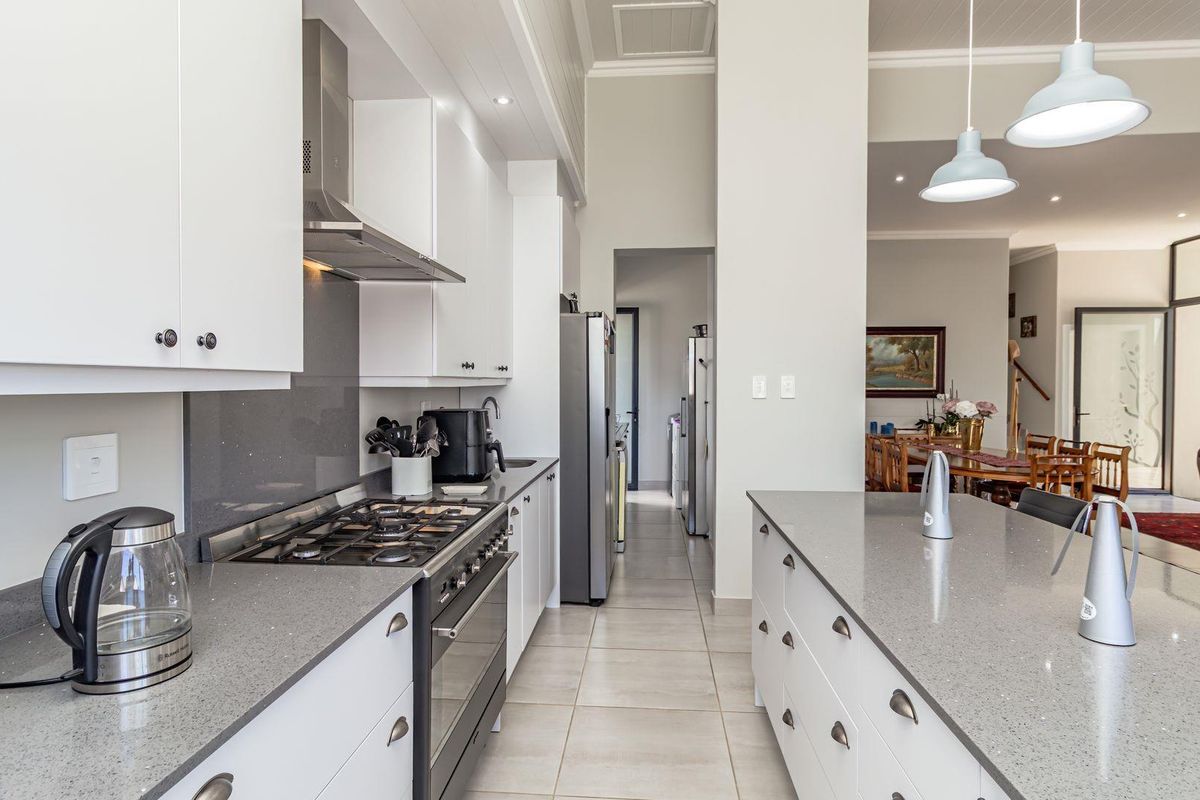 Modern kitchen featuring stone countertops, a gas cooktop with stainless steel extractor, and a central island, flowing into an open-plan living and dining area.