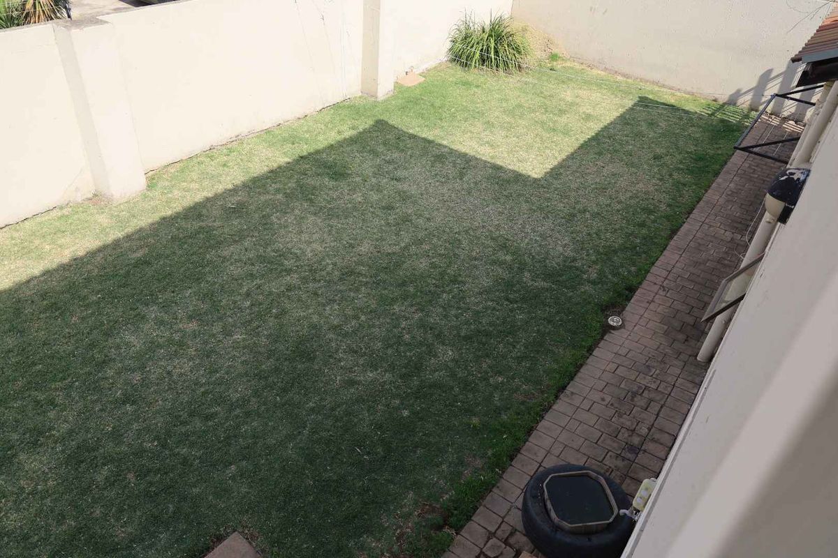 A private rear garden featuring a lawn area and paved walkway, enclosed by high boundary walls.