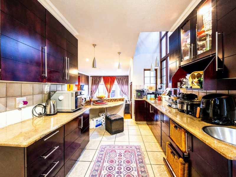 A galley-style kitchen featuring dark wood cabinetry, granite countertops, tiled flooring, and a tiled backsplash, leading into an open-plan living area.