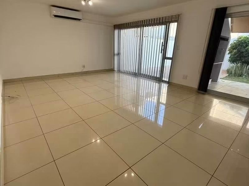 Spacious, light-filled living area featuring polished tile flooring, a wall-mounted air conditioning unit, and large sliding glass doors leading to an outdoor space.