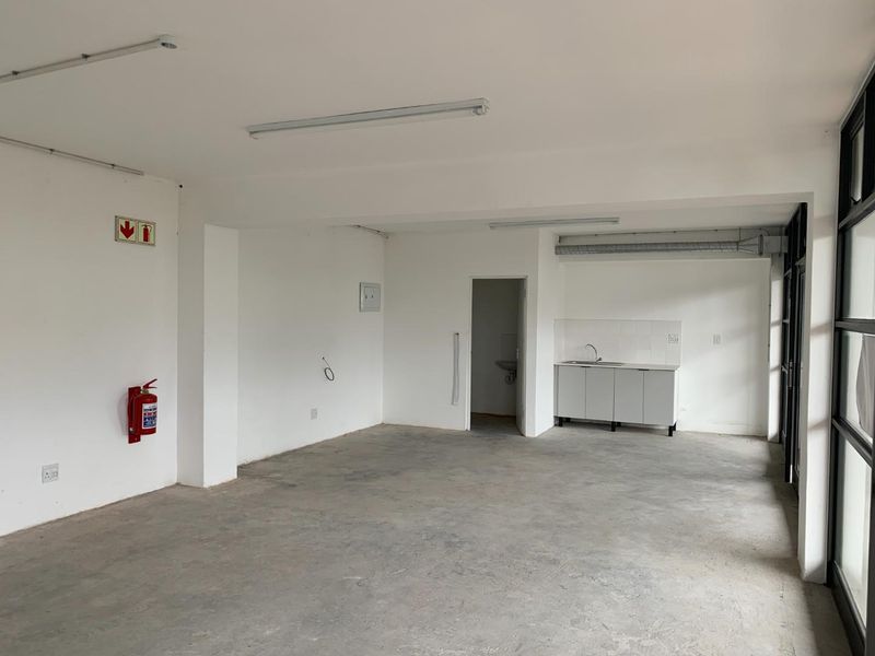 An open-plan commercial or utility space featuring a basic kitchenette, concrete flooring, and large glass doors, suitable for various business or office uses.