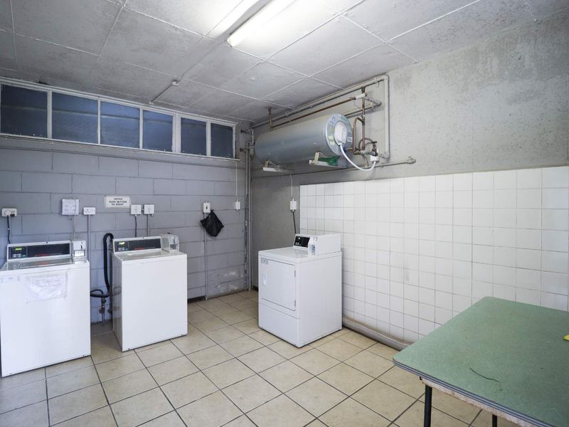 Functional laundry room featuring tiled flooring, exposed blockwork walls, and a wall-mounted electric water heater.