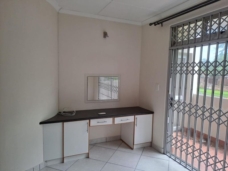 A bedroom featuring a built-in vanity unit, tiled flooring, and a sliding door with a security gate leading to the exterior.