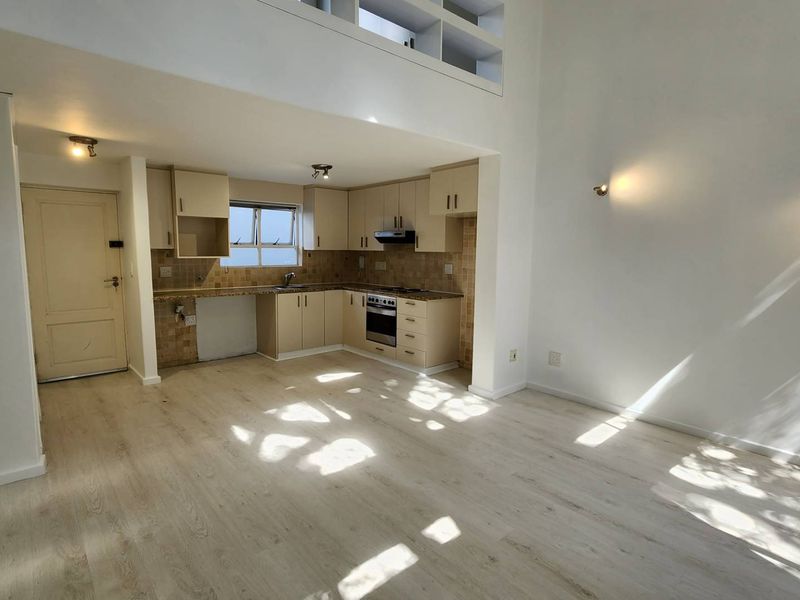 Spacious open-plan living area featuring a functional kitchen with built-in cabinetry, oven, and hob, complemented by light laminate flooring and a mezzanine level.