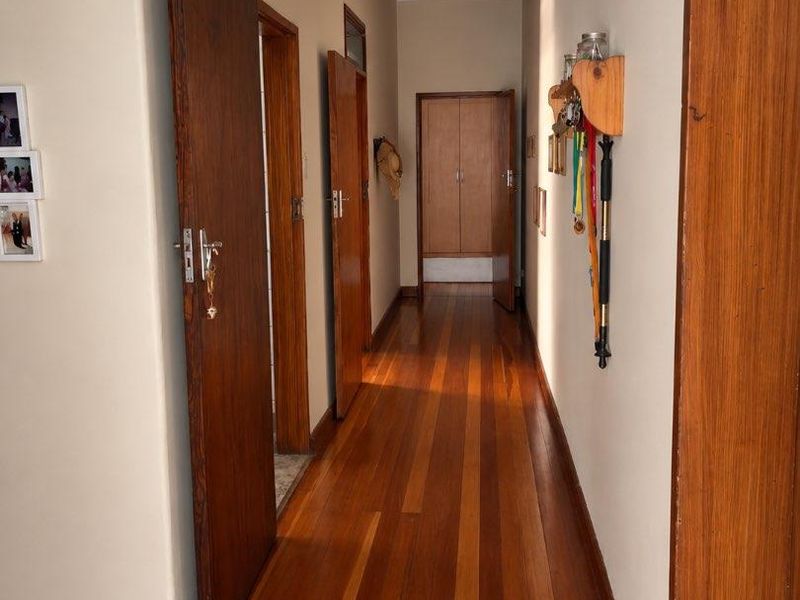 A well-maintained hallway featuring polished hardwood flooring, classic wooden door frames, and a built-in storage cupboard at the end of the passage.